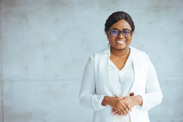 Portrait of beautiful confident smiling african-american businesswoman standing with arms crossed in the office and looking at camera. Smiling African American business woman wearing stylish eyeglasses looking at camera