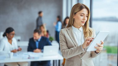 Urban happy business woman using tablet computer and working. Happy businesswoman using a digital tablet. Young leading businesswoman using a wireless tablet. Designer standing in her office using an online app clipart