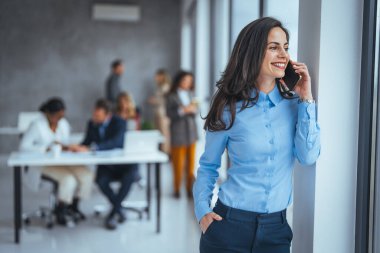 Ofiste telefonla gülümseyen bir iş kadını. Cep telefonuna bakıp gülümseyen küçük bir girişimci. Güzel gülümseyen iş kadını akıllı telefonu içeride kullanıyor, boşluğu kopyalıyor..