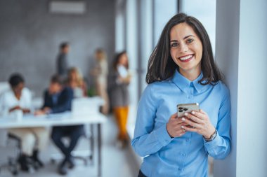 Ofiste telefonla gülümseyen bir iş kadını. Cep telefonuna bakıp gülümseyen küçük bir girişimci. Güzel gülümseyen iş kadını akıllı telefonu içeride kullanıyor, boşluğu kopyalıyor..