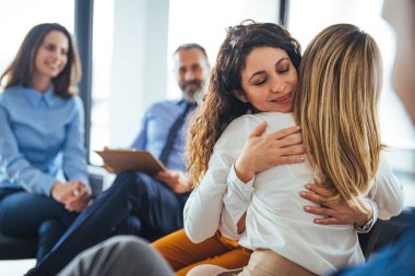 Genç yetişkin bir kadın, çeşitli kadınlarla grup terapisi sırasında arkadaşını kucaklıyor ve destekliyor. Terapi seansında iki kadın sarılıyor. Grup terapi oturumu, empati konsepti