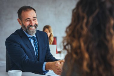 Mutlu kıdemli girişimci, iş arkadaşıyla ofiste yapacağı bir toplantıda anlaşmaya vardı. Ofiste iş görüşmesi yapan mutlu işadamları. Olgun bir iş adamının bir adayla el sıkışmasına odaklan..