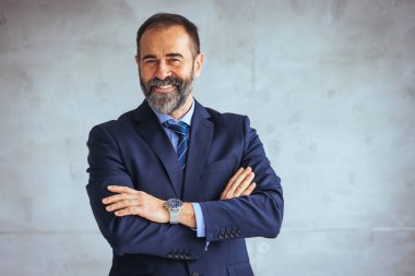 Mature businessman portrait. Successful businessman posing with crossed arms and smiling at camera. Good-looking middle-aged businessman with arms crossed isolated in gray background clipart