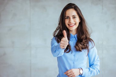 Mutlu iş kadını gri arka planda baş parmağını gösteriyor. Mavi gömlekli olan. Kameraya bakıyorum. Gibi. Neşeli Ofis Kızı Gri Arkaplanda Ayakta İşaret Ediyor. Stüdyo Çekimi