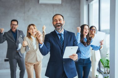 Başarılı bir iş grubu ofiste elde edilen başarıyı kollarını kaldırıp kameraya gülümseyerek kutluyor. Bir grup genç iş adamının modern bir ofiste dayanışma içinde toplanması.