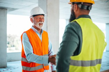 İnşaat alanında erkek mühendisler veya mimarlar el sıkışıyor 