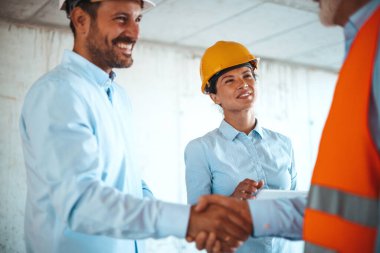 Kadın mimar veya mühendis inşaat alanında erkek meslektaşlarının el sıkışmalarına bakıyor. 