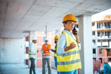 Kafkasyalı iş kadını iş sırasında telefonda konuşuyor. Sarı batıdaki muhteşem beyaz kadın mimar ve inşaat alanında duran ve akıllı telefon kullanan koruyucu kasklı..