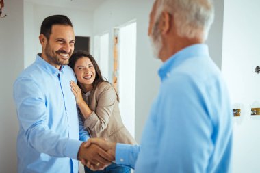 Mutlu çift yeni bir ev alıyor ve emlakçılarıyla tokalaşıyor. Ev ziyareti sırasında emlakçı çifti selamlıyor. Çift emlak acentesi ev emlak işi yatırım satın alıyor