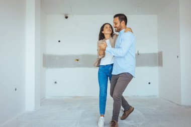 Apartman seçiminde mutlu dans eden çift. Yer değiştirme, emlak, kira konsepti. Mutlu ve heyecanlı genç çift yeni aldıkları şeylere bakınıyor.