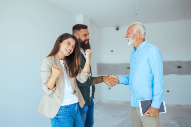Erkek emlakçı genç bir çifte satılık bir daire gösteriyor. Emlakçı Genç Bir Çifte Parlak Yeni Daire Gösteriyor. Emlakçı genç bir çifte ev satıyor. 