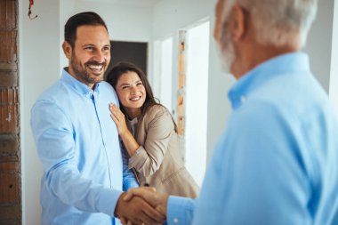 Erkek emlakçı genç bir çifte satılık bir daire gösteriyor. Emlakçı Genç Bir Çifte Parlak Yeni Daire Gösteriyor. Emlakçı genç bir çifte ev satıyor. 