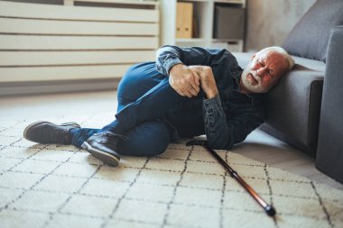 Yaşlı kıdemli adam kayıyor ve düşüyor. Oturma odasında düşen yaşlı insan. Yaşlı adam halının üzerine düşüyor ve evde oturma odasında yere uzanıyor, yaşlı yetişkin konsepti şelaleleri.