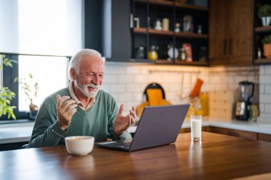 Kahvaltıda ve kahve içerken dizüstü bilgisayarda yazan olgun bir adam. Evden çalışan emekli yaşlı bir insan, uzaktan internet üzerinden modern iletişimi kullanarak evden işe gidiyor.
