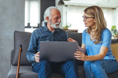 Dost canlısı, genç bir hemşire engelli bir adama evde yardım ediyor dizüstü bilgisayar başında oturuyor, sohbet ediyor, gülümsüyor, alet ekranına dokunuyor.