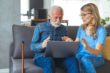 Nurse help senior man with internet and laptop on the sofa in a retirement home. Healthcare worker, caregiver or medical professional helping retired man with email and technology in the lounge