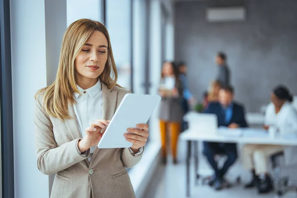 Portrait of happy blond businesswoman using digital tablet in agency. Successful business woman in casual clothing working on tablet. Mixed race young woman looking at camera in creative office.