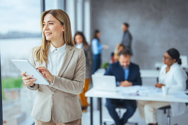 Портрет счастливой блондинки-предпринимательницы, использующей цифровой планшет в агентстве. Успешная деловая женщина в повседневной одежде работает на планшете. Молодая женщина смешанной расы смотрит в камеру в креативном кабинете.