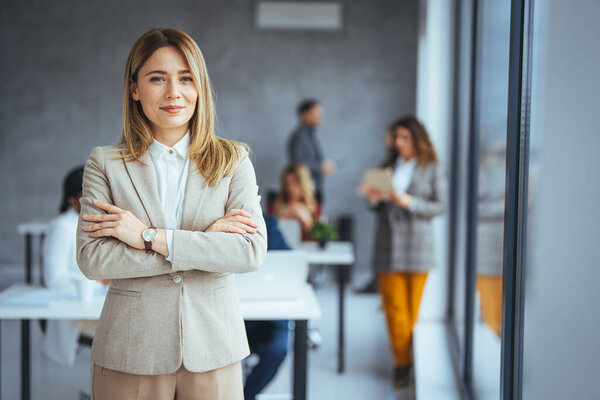 Portrait of businesswoman with a file standing in meeting room with colleagues disucssing in background. Waist up portrait modern business woman in the office with copy space