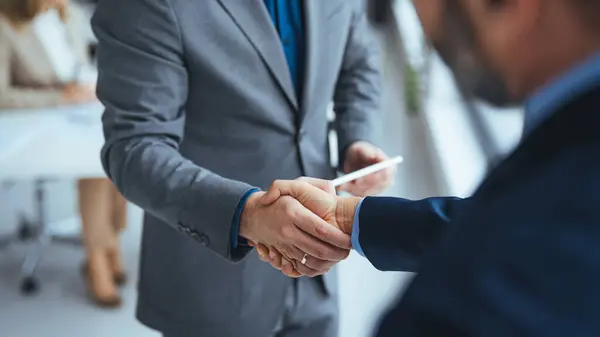 Business people in office suits standing and shaking hands, close-up. Business communication concept. Handshake and marketing. Two smiling businessmen shaking hands