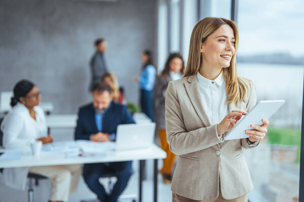 Застрелен молодой бизнесвумен с помощью цифрового планшета. Снимок деловой женщины, использующей цифровой планшет за своим столом в современном офисе. Портрет улыбающейся молодой предпринимательницы с планшетом в офисе 