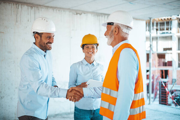 Woman architect or engineer looking at male colleagues handshaking at construction site 