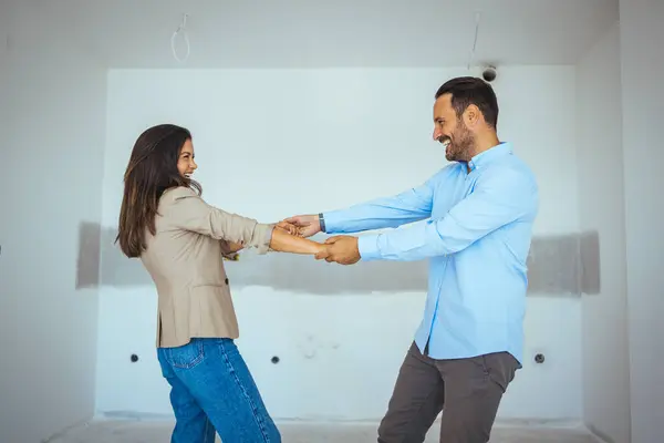 Dancing Couple Happy With Apartment Choice. Relocation, real estate, rent concept. Happy and Excited Young Couple Look Around In Wonder at their Newly Purchased