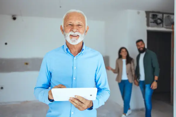 Male real estate agent holding a tablet and looking at camera smiling very happy. Happy real estate agent showing a house. Real estate agent at his work