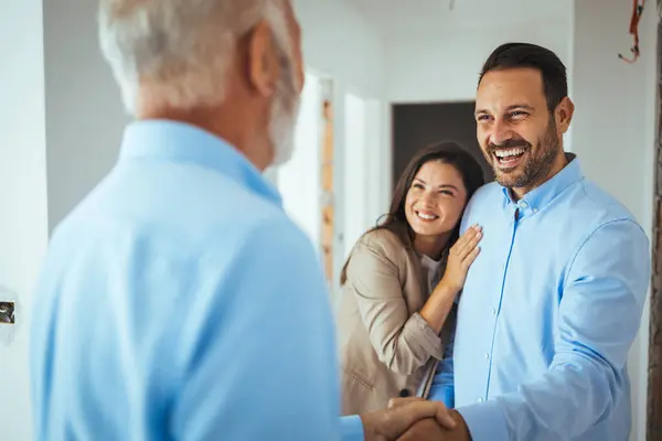 Friendly Real Estate Agent and young couple shaking hands standing in hallway, real estate agent handshaking clients at meeting, showing selling buying property for rent sale, discussing deal with customers