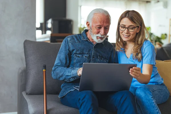 Nurse help senior man with internet and laptop on the sofa in a retirement home. Healthcare worker, caregiver or medical professional helping retired man with email and technology in the lounge