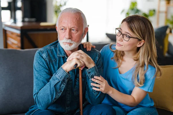 Community Nurse Visits Senior Man Suffering With Depression. A woman carer concerned about an elderly man looking depressed. Desperate sad pensioner living in residential home