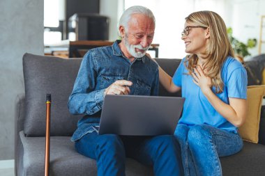 Dost canlısı, genç bir hemşire engelli bir adama evde yardım ediyor dizüstü bilgisayar başında oturuyor, sohbet ediyor, gülümsüyor, alet ekranına dokunuyor.