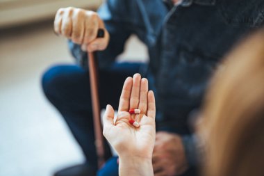 Genç bir hemşire yaşlı bir adamla oturma odasında bir masada oturuyor ve ona tıbbi yardım sağlıyor. Kanepede oturan yaşlı hastaya ilaç veren kadın doktor.