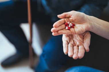 Genç bir hemşire yaşlı bir adamla oturma odasında bir masada oturuyor ve ona tıbbi yardım sağlıyor. Kanepede oturan yaşlı hastaya ilaç veren kadın doktor.