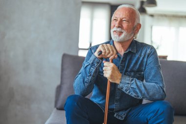 Evde kanepede oturan sakat sopalı yaşlı adam.