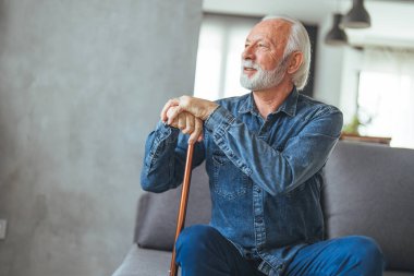Evde kanepede oturan sakat sopalı yaşlı adam.