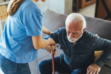 Hemşire engelli ihtiyara yardım ediyor. Evdeki kanepeden kalkmış sopa yiyor.