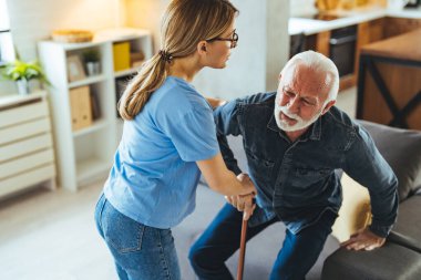 Hemşire engelli ihtiyara yardım ediyor. Evdeki kanepeden kalkmış sopa yiyor.