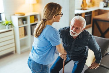 Hemşire engelli ihtiyara yardım ediyor. Evdeki kanepeden kalkmış sopa yiyor.