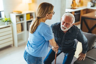Hemşire engelli ihtiyara yardım ediyor. Evdeki kanepeden kalkmış sopa yiyor.