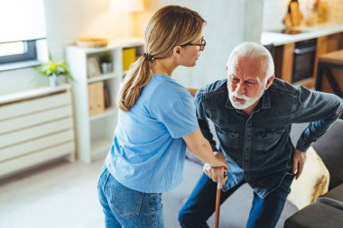 Hemşire engelli ihtiyara yardım ediyor. Evdeki kanepeden kalkmış sopa yiyor.