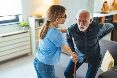 Hemşire engelli ihtiyara yardım ediyor. Evdeki kanepeden kalkmış sopa yiyor.
