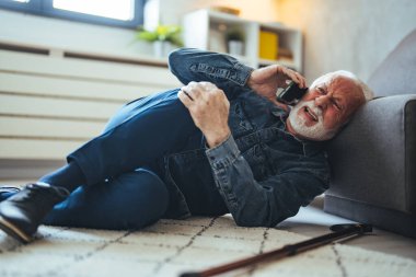 Olgun, beyaz bir adam. Acı içinde yerde yatıyor ve evdeki kanepenin yanında akıllı telefondan konuşuyor.