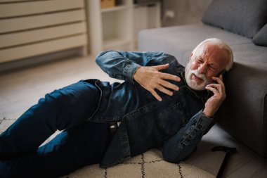 Olgun, beyaz bir adam. Acı içinde yerde yatıyor ve evdeki kanepenin yanında akıllı telefondan konuşuyor.