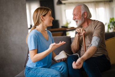 Genç bayan hemşire evdeki kanepede engelli sopalı yaşlı adamın baskısını ölçüyor.