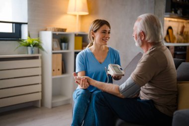 Genç bayan hemşire evdeki kanepede yaşlı adamın baskısını ölçüyor.