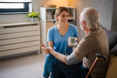 Genç bayan hemşire evdeki kanepede yaşlı adamın baskısını ölçüyor.