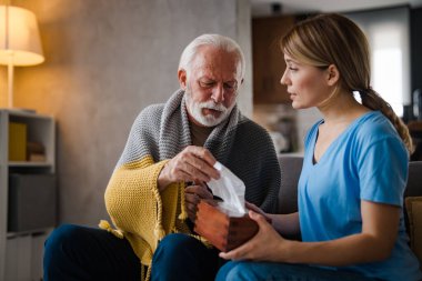 Hasta, olgun bir adam, evdeki kanepedeki genç kadın hemşirenin elinde tahta kutudan peçete alıyor.