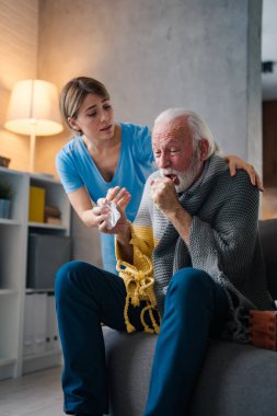 Hasta olan genç bayan hemşire. Evde kanepede öksüren peçeteli olgun bir adam.