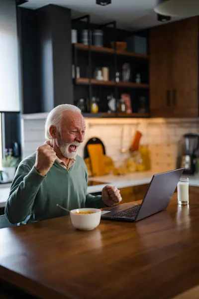 Happy excited old elderly man winner excited by reading good news looking at laptop, overjoyed senior mature grandfather watching game online celebrating goal bid bet win great result victory concept
